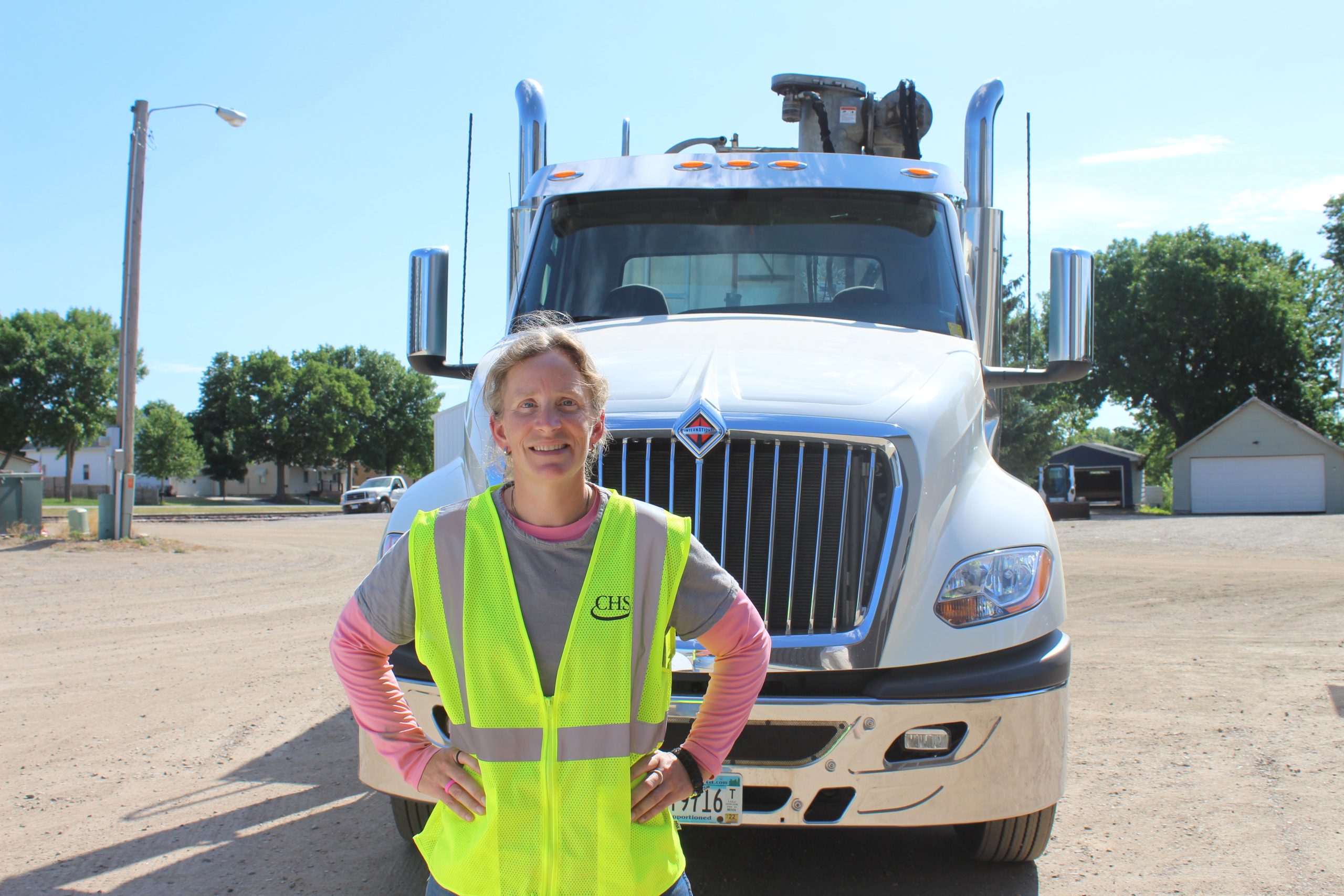 Woman in a yellow safety vest standing in front of a parked semi truck